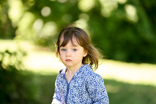 Pensive toddler girl with brown hair and blue eyes in a parkland.