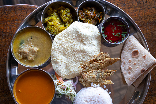 This image presents a lavish spread of Indian cuisine, beautifully arranged on a traditional silver platter. The array includes a variety of dishes that are central to Indian gastronomy: crispy poppadoms, a selection of vibrant chutneys, rich and flavourful curries, and freshly made chapatis. Each element of the meal is carefully placed to showcase the diversity and colour of the dishes. The photograph aims to capture the essence of Indian dining, where a mix of textures, flavors, and aromas come together to create a feast not just for the palate but also for the eyes. This image encapsulates the communal and celebratory spirit of Indian meals, highlighting the cultural significance of food in bringing people together.