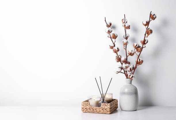 istock Burning candles in wicker basket and vase with cotton branches on table against white background. Space for text 1802762310