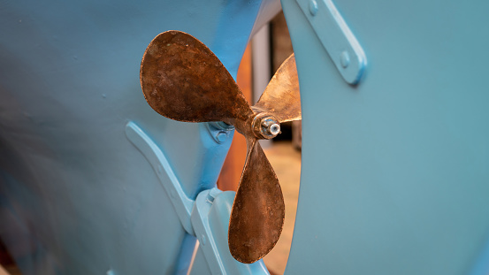 The rudder and propeller of a blue boat in dry dock