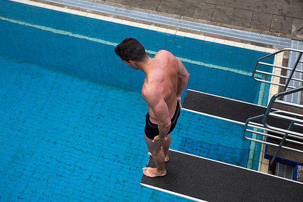 Man with fear of height standing on diving board at public swimming pool above the water