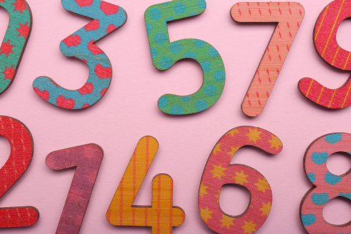 Colorful wooden numbers on pink background, flat lay