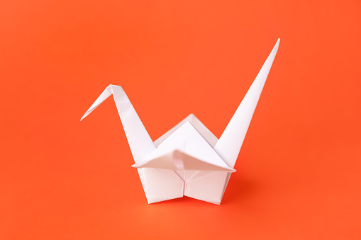 Origami art. Handmade paper crane on orange background, closeup