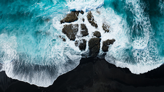 Breaking Waves of the Atlantic Ocean on the Coast of Lanzarote. Rocky Black Volcanic Lava Beach. Aerial Drone Point down towards the lava volcanic rocks and breaking turquoise waves. Black volcanic sand beach, Lanzarote Island, Canary Islands, Spain - Africa