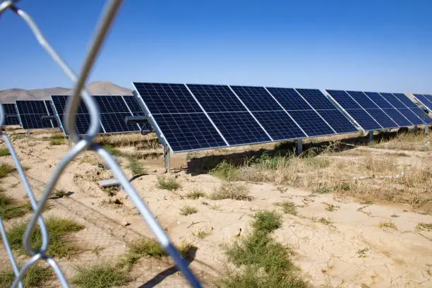 Solar panels under the blue sky in the barren land behind the fence