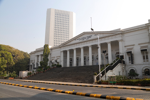 This image captures the grandeur of the Asiatic Library in Mumbai, an iconic landmark known for its neoclassical architecture and rich cultural heritage. Situated in the bustling area of Fort, Mumbai, the library's majestic steps and the imposing structure are prominently featured in the photograph. The building's elegant façade, characterized by its white exterior and Grecian columns, reflects the city's colonial past and its affinity for classical architectural styles. The photograph aims to highlight the library's status as a center for scholarly pursuits and a repository of rare books and manuscripts, making it a beacon of knowledge and history in the heart of Mumbai. The Asiatic Library not only stands as a testament to the city's intellectual legacy but also as a symbol of architectural beauty and historical significance.