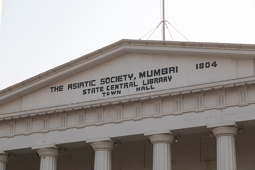 This image captures the grandeur of the Asiatic Library in Mumbai, an iconic landmark known for its neoclassical architecture and rich cultural heritage. Situated in the bustling area of Fort, Mumbai, the library's majestic steps and the imposing structure are prominently featured in the photograph. The building's elegant façade, characterized by its white exterior and Grecian columns, reflects the city's colonial past and its affinity for classical architectural styles. The photograph aims to highlight the library's status as a center for scholarly pursuits and a repository of rare books and manuscripts, making it a beacon of knowledge and history in the heart of Mumbai. The Asiatic Library not only stands as a testament to the city's intellectual legacy but also as a symbol of architectural beauty and historical significance.