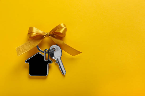 istock Key with trinket in shape of house and bow on yellow background, top view. Space for text. Housewarming party 1802802480