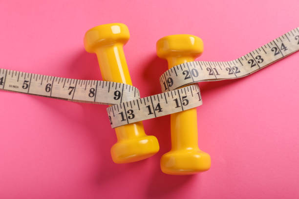 istock Measuring tape and dumbbells on pink background, flat lay. Weight control concept 1802805071