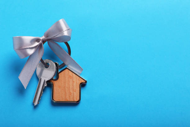 istock Key with trinket in shape of house and bow on light blue background, top view. Space for text. Housewarming party 1802805151