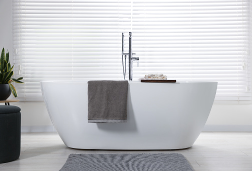 Stylish bathroom interior with ceramic tub, terry towels and houseplant