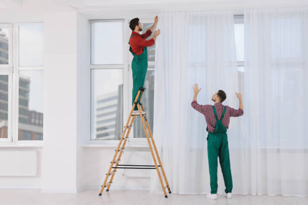 Workers in uniform hanging window curtain indoors
