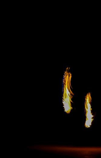 Two torch flames against a black backdrop held by a unseen fire spinner on right bottom section of photo