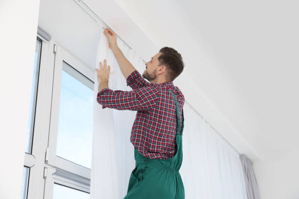 istock Worker in uniform hanging window curtain indoors, low angle view 1802830684