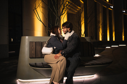 couple in love sits on a bench in the evening in the city, a date in winter.