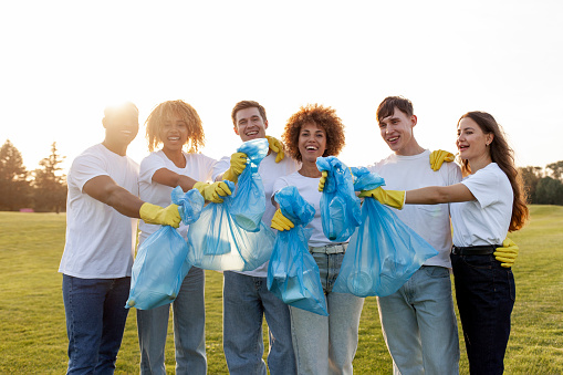 multiracial group of people volunteers in gloves with garbage bags collect garbage and plastic in the park, team of students help green the planet, youth take care of the environment