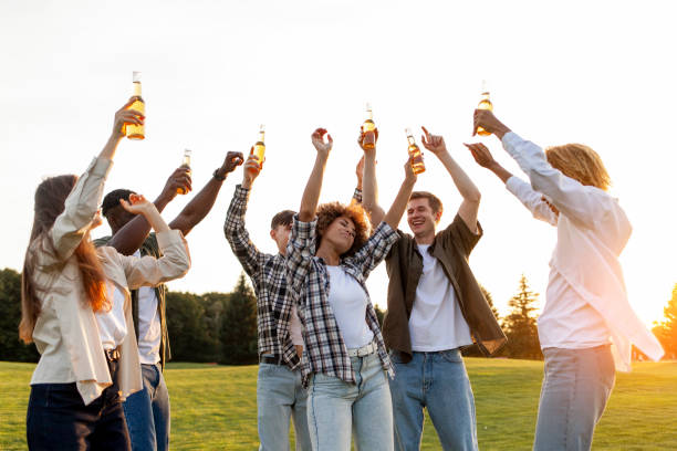 groupe d’amis multiraciaux à la fête avec des bouteilles de bière dansant et s’amusant à l’extérieur, groupe de personnes chantant - music festival park friendship summer photos et images de collection