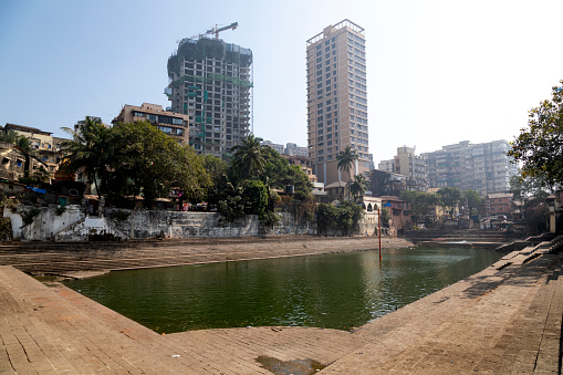 This image features Banganga Tank, a deeply historical and spiritual site nestled in the Walkeshwar Temple Complex in Mumbai. The tank, flanked by stone steps and surrounded by ancient temples and residential buildings, provides a tranquil oasis amid the bustling city. In the photograph, the serene water of the tank contrasts with the vibrant life along its banks, where local residents engage in daily rituals and activities. The image aims to capture the timeless essence of Banganga, highlighting its significance as both a cultural heritage site and a vital element of the local community. It offers a glimpse into the blend of spirituality, history, and everyday life that defines this unique corner of Mumbai.