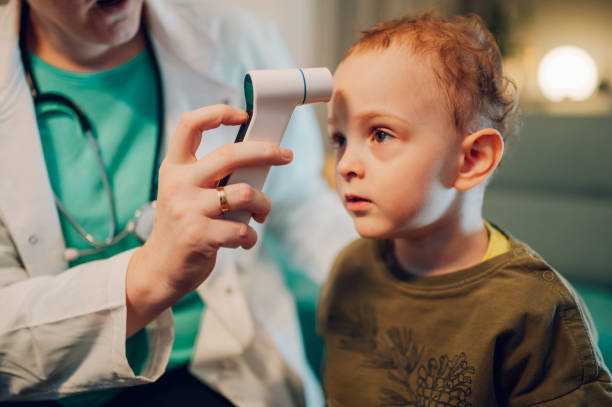 istock A boy is sitting at home while doctor is using thermometer on his forehead. 1802840953