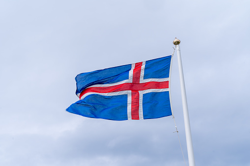 The flag of the United Kingdom of Great Britain and Northern Ireland, known as Union Flag or Union Jack, hanging down loosely at full-mast on a white pole against blue sky.