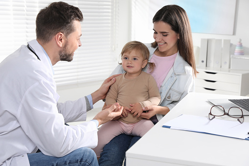 Mother and her cute baby having appointment with pediatrician in clinic. Doctor examining little girl