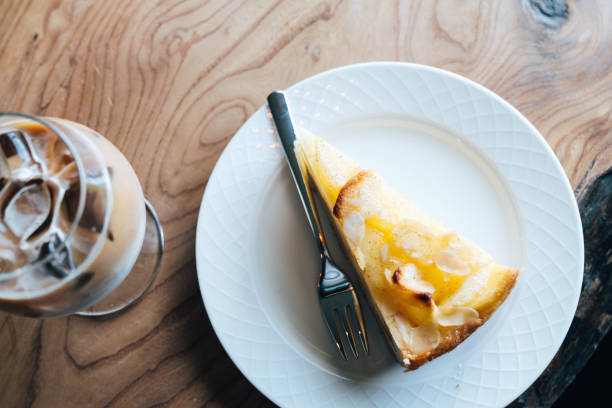 Cheesecake on a white plate on a wood table with an iced coffee beverage, defocused