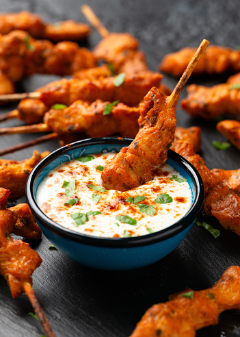 Grilled chicken fillet on skewers with white sauce on rustic stone board.