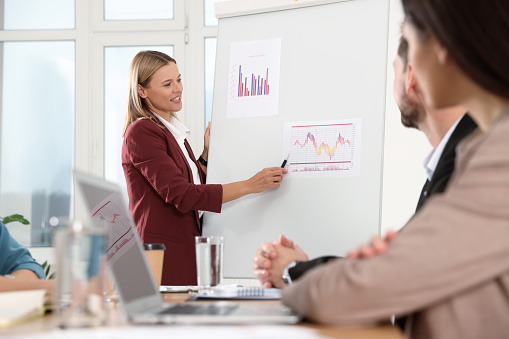 Businesswoman showing charts near flipchart on meeting in office