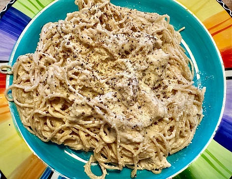 Plate of white pesto pasta with chicken, basil and Parmesan cheese.