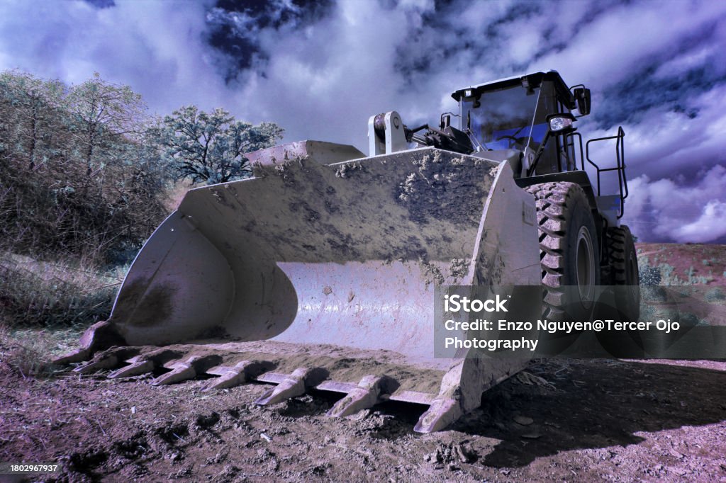 Bulldozer on construction site facing with bucket laying on the ground with clouds in the sky Archaeology Stock Photo