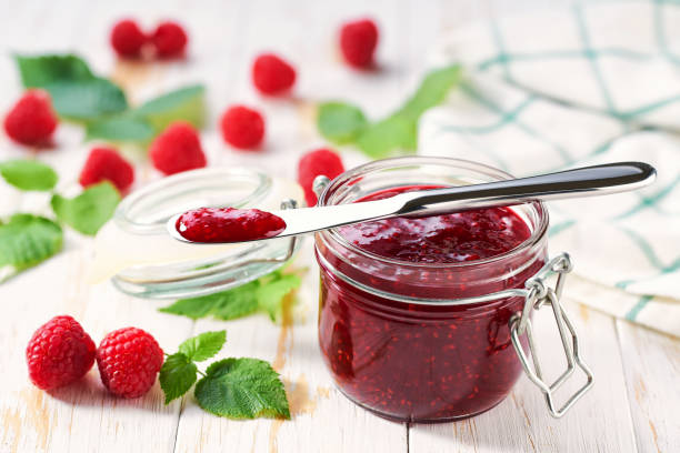istock Sweet raspberry jam in jar with fresh berries on wooden table. Delicious raspberry jam on table close-up. 1802986319