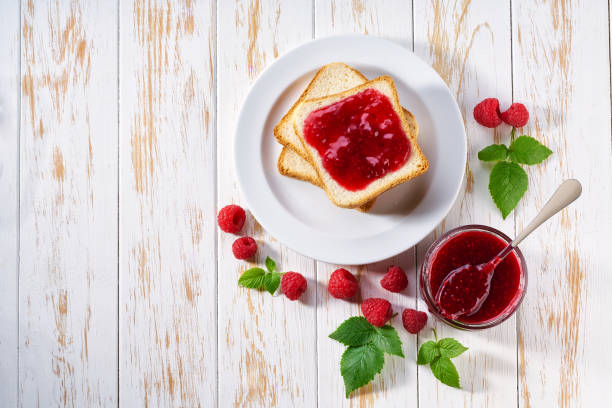 istock Toasts of bread with raspberry jam and fresh berries  on white wooden table. Top view. 1802986340