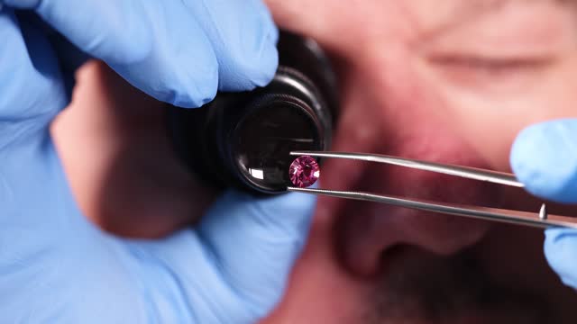 Jeweler looking at magnifying glass at pink diamond on tweezers closeup 4k movie slow motion