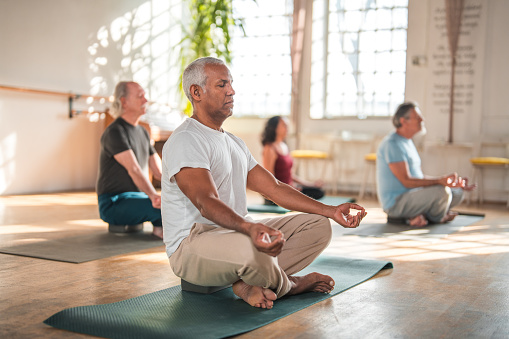 A diverse group of happy retirees in comfortable workout clothes participating in a yoga class led by a young instructor. The seniors are happily stretching and performing yoga poses, and meditation emphasizing the importance of fitness and well-being in later life.