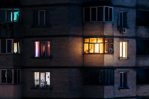 warm light from the balcony window at evening time\ncozy atmosphere\nphoto of soviet era brick residential house facade