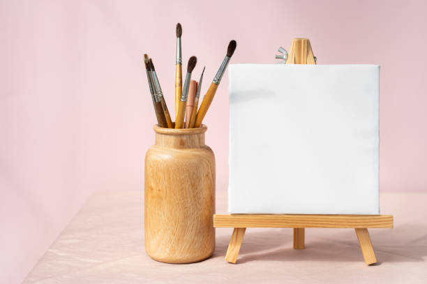 istock Easel with blank canvas and vase with brushes. Artistic still life. 1803025732