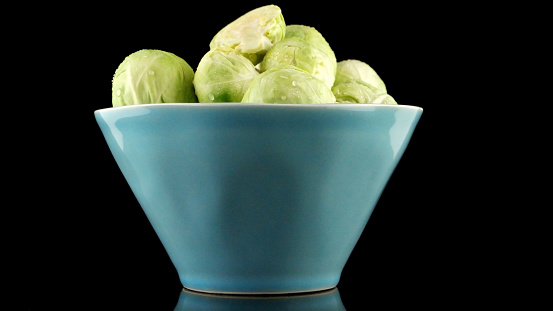Fresh brussels sprouts on blue ceramic bowl isolated on black background.