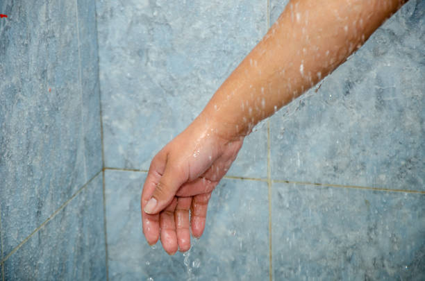 unrecognizable woman holding her hands under running water against a blue wall