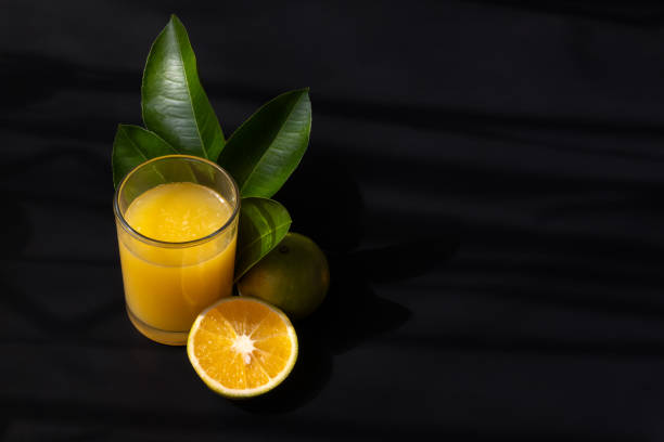 istock Orange juice, leaves and fruit with a black background and space for text on the right side 1803096629