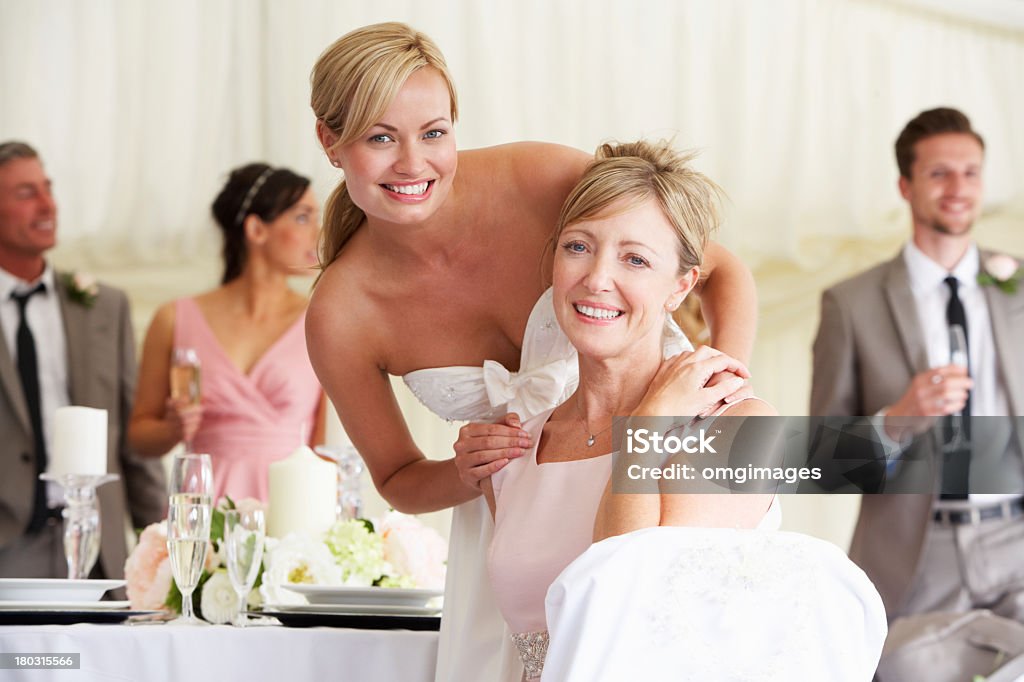 A young bride with her mother at a wedding reception Bride With Mother At Wedding Reception Smiling To Camera Mother of the Bride Stock Photo