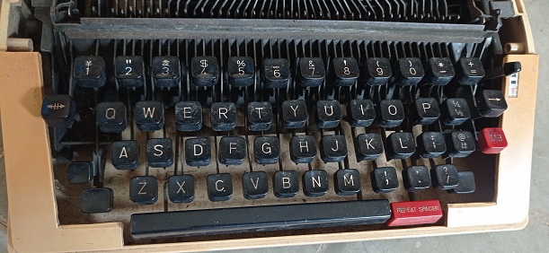 Old-fashioned typewriter sitting on a desk, with copy space on the blank paper and on the background.