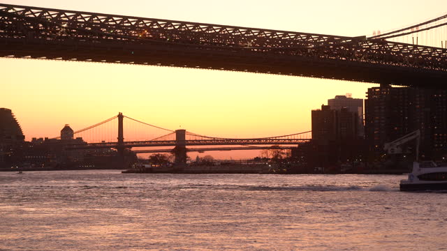 Ferry boat crossing the East River with view of Williamsburg Bridge and Brooklyn Bridge at sunset, New York City