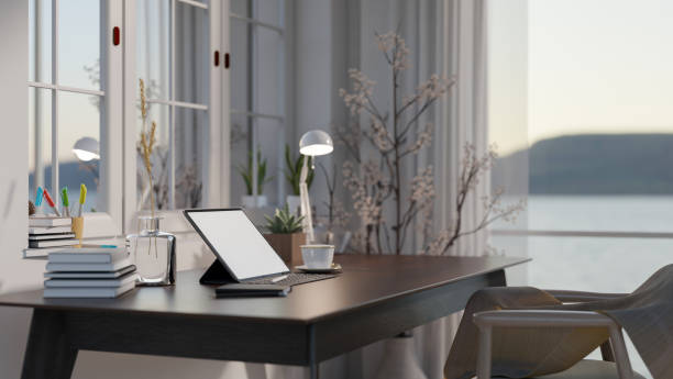 istock Minimal cozy home office space with blank screen mock up tablet on dark wooden table, large window with sea view. 1803245560