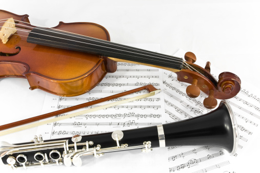 Two musical instrument for classical music, a violin part with his bow and a clarinet bottom part. Isolated on white background with printed sheet music.