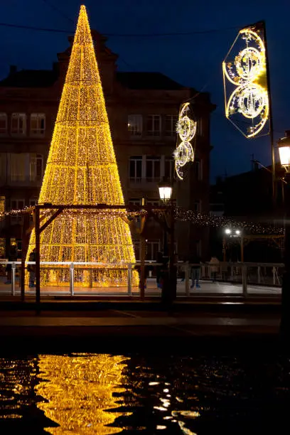Modern Christmas tree, Christmas lights reflected on pond at dusk, ice-skating. Vigo, Pontevedra province, Galicia,