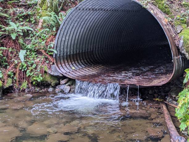istock Iron culvert draining water into a clear pond 1803425398