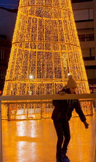 Modern Christmas tree, Christmas lights reflected at dusk, ice-skating town square. Vigo, Pontevedra province, Galicia, Spain.