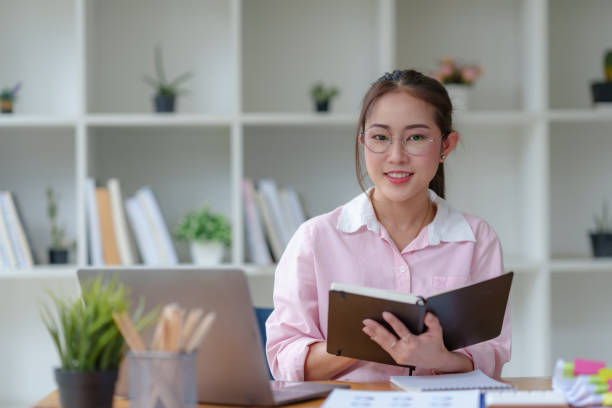 istock Young Asian businesswoman using laptop computer, taking notes, working project in modern office. Financier working with documents at workplace. 1803450929