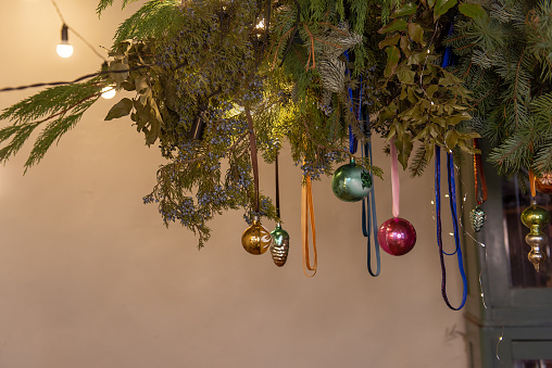 Authentic creative botanical Christmas rustic interior design. Hanging garland of green fir branches with Christmas balls on ribbons. Vintage bright garlands