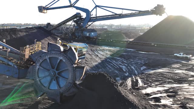 Industrial coal mine with conveyor belts and large wheel excavator. Aerial tracking shot of coal shipping and distribution at port.